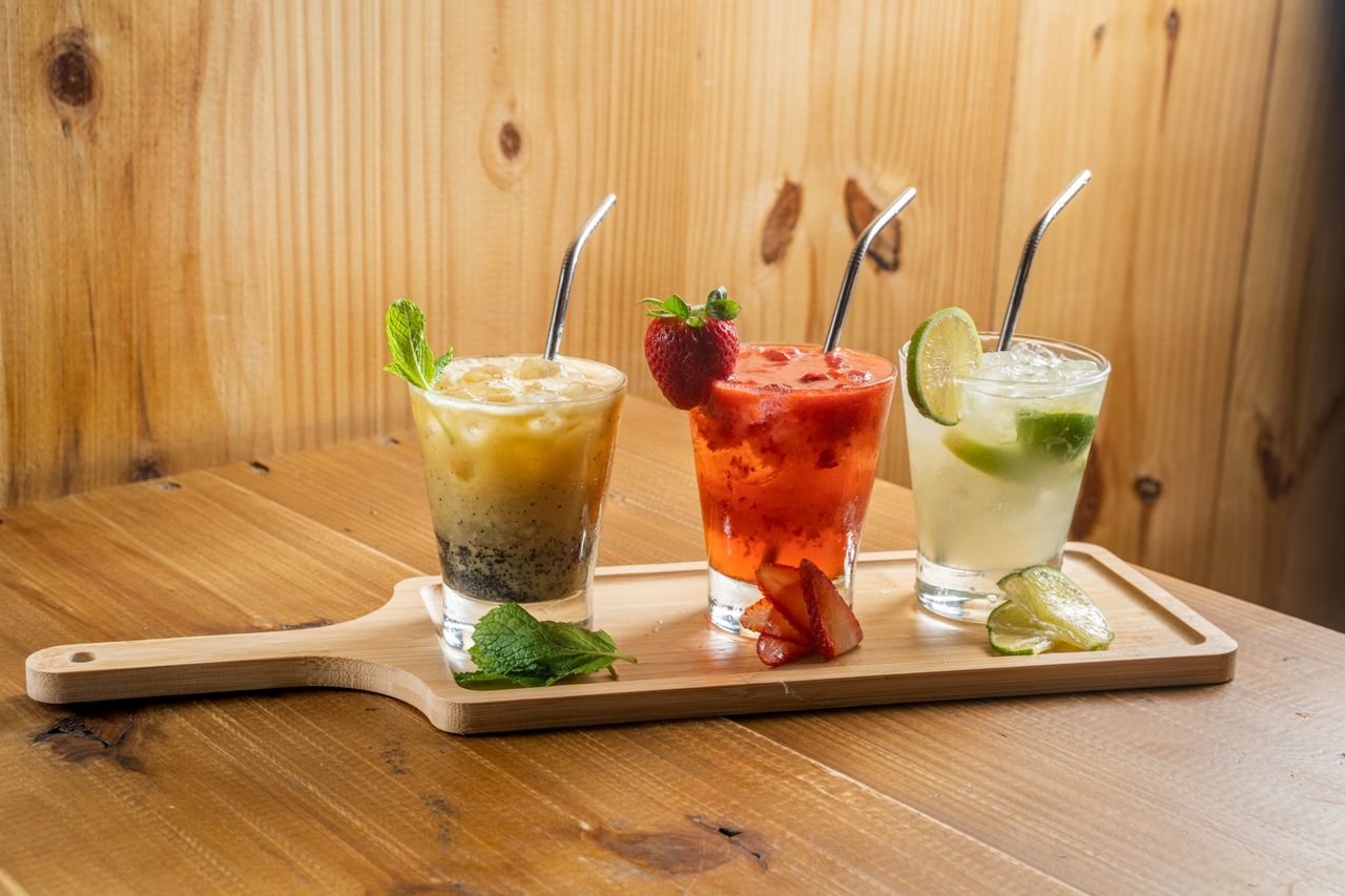 Contact Three colorful cocktails with fruits on a wooden board, perfect for summer refreshment.