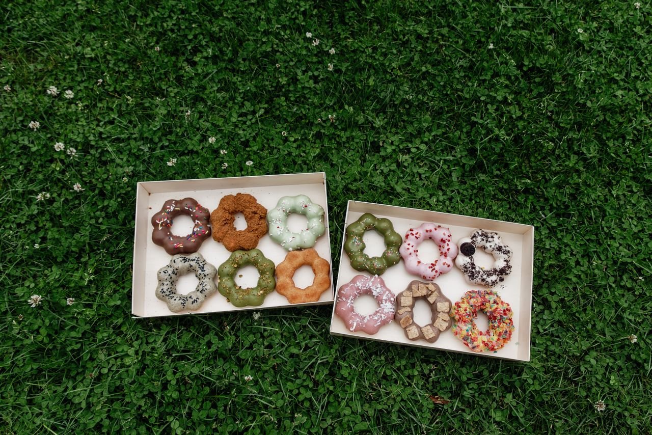 About Boxes of decorative ring-shaped donuts placed on lush green grass, offering a colorful selection.