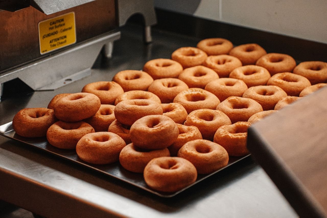 Tray of freshly baked donuts cooling on a stainless steel counter in a bakery kitchen.