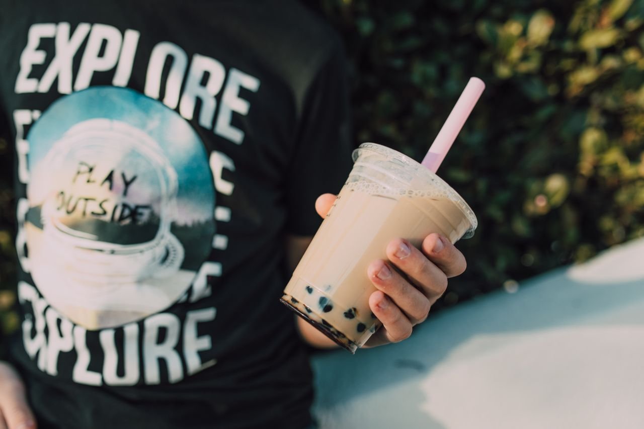 Services Close-up of a person holding delicious bubble tea outdoors, with vibrant surroundings.