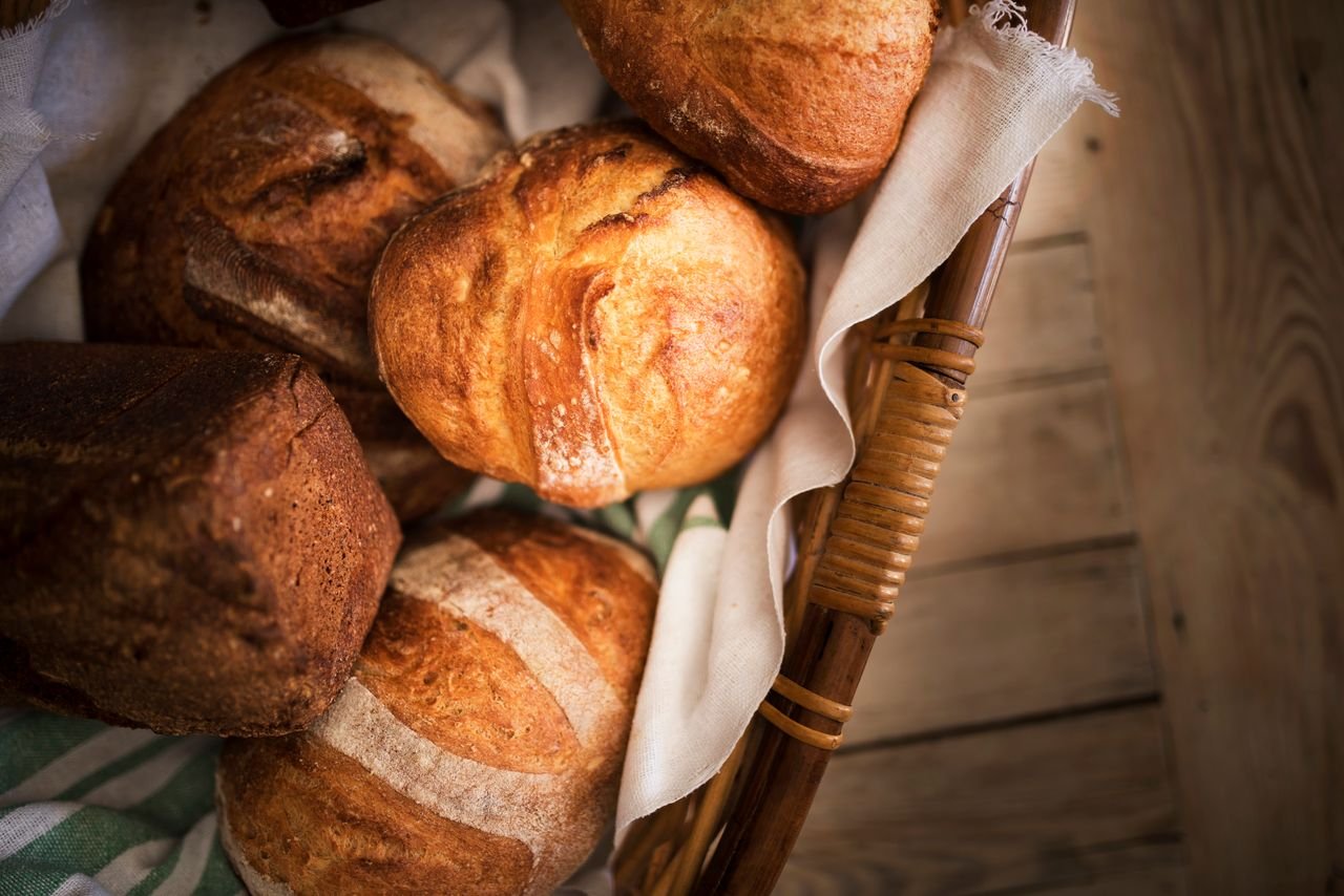 Services From above of fresh baked buns with fresh sourdough bread placed in basket on blurred background of wooden surface in bakery
